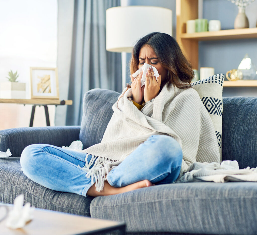 Sick female sitting on couch testing for COVID, Flu, and strep with My Labs Direct At-Home Test Kit